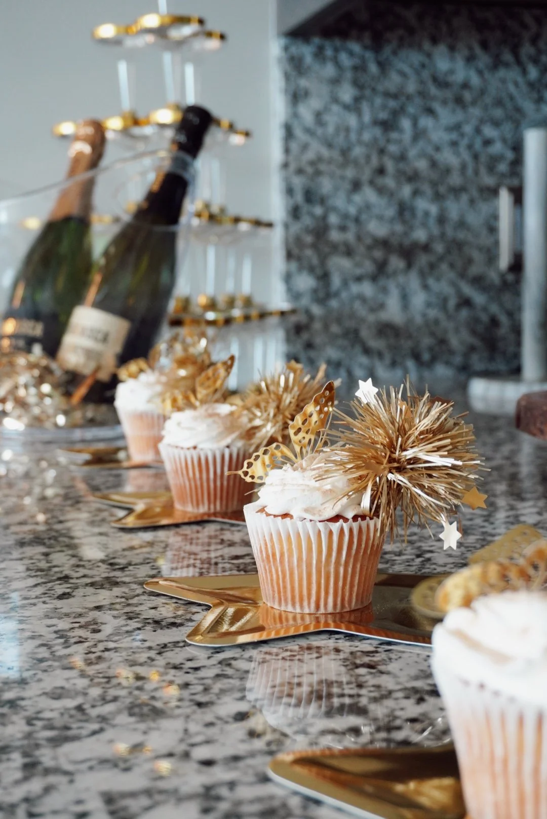 Cupcakes decorated with gold and white festive embellishments on a granite countertop.