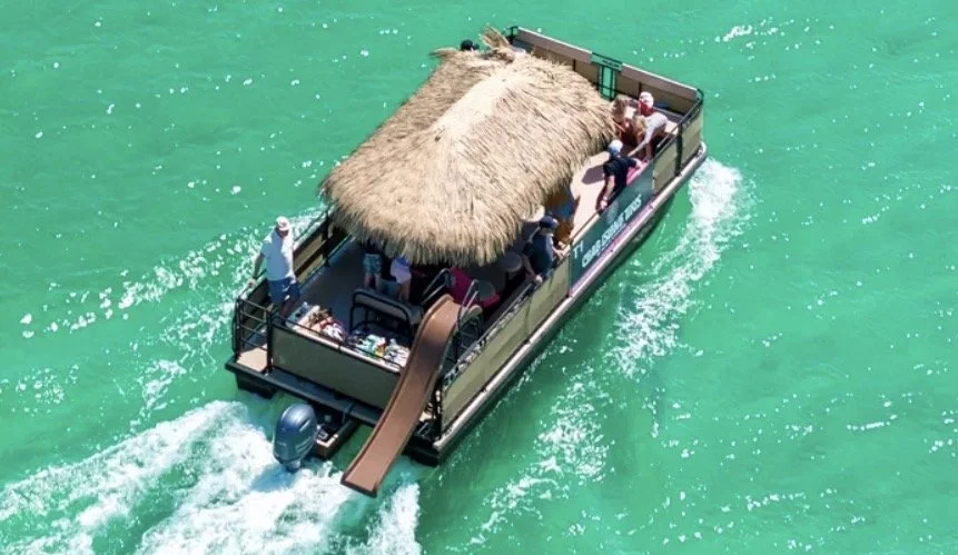 Tourist boat with a thatched roof and open sides, carrying passengers on turquoise water.