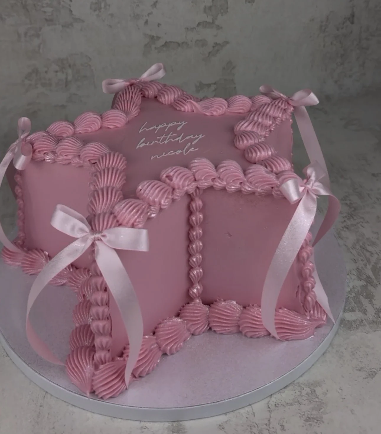 Pink birthday cake decorated to look like a gift box with ribbon and bow, with the message 'happy birthday nose' written on top.