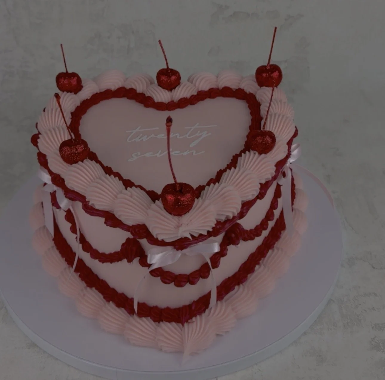 Pink heart-shaped cake decorated with red cherries and pink icing, with the words 'twenty seven' written on top.