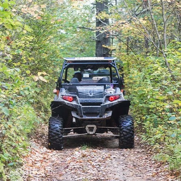Off-road utility vehicle driving down a dirt trail surrounded by green foliage and trees.