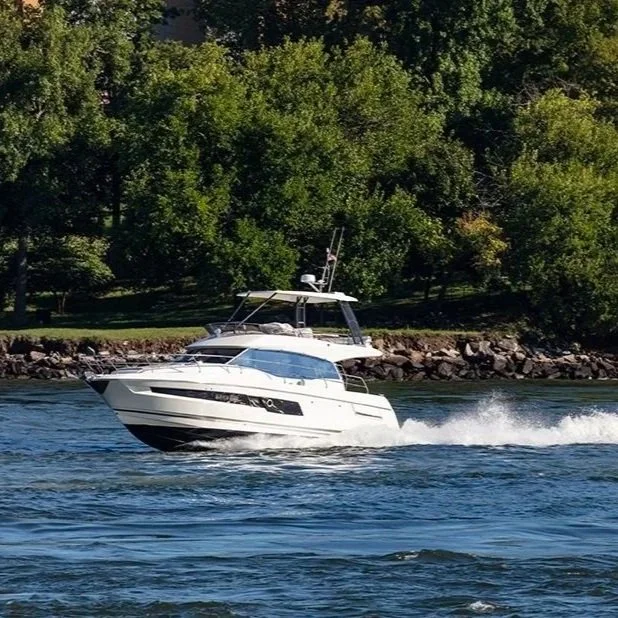 A white motor boat moving quickly on a body of water with trees and rocks along the shoreline in the background.