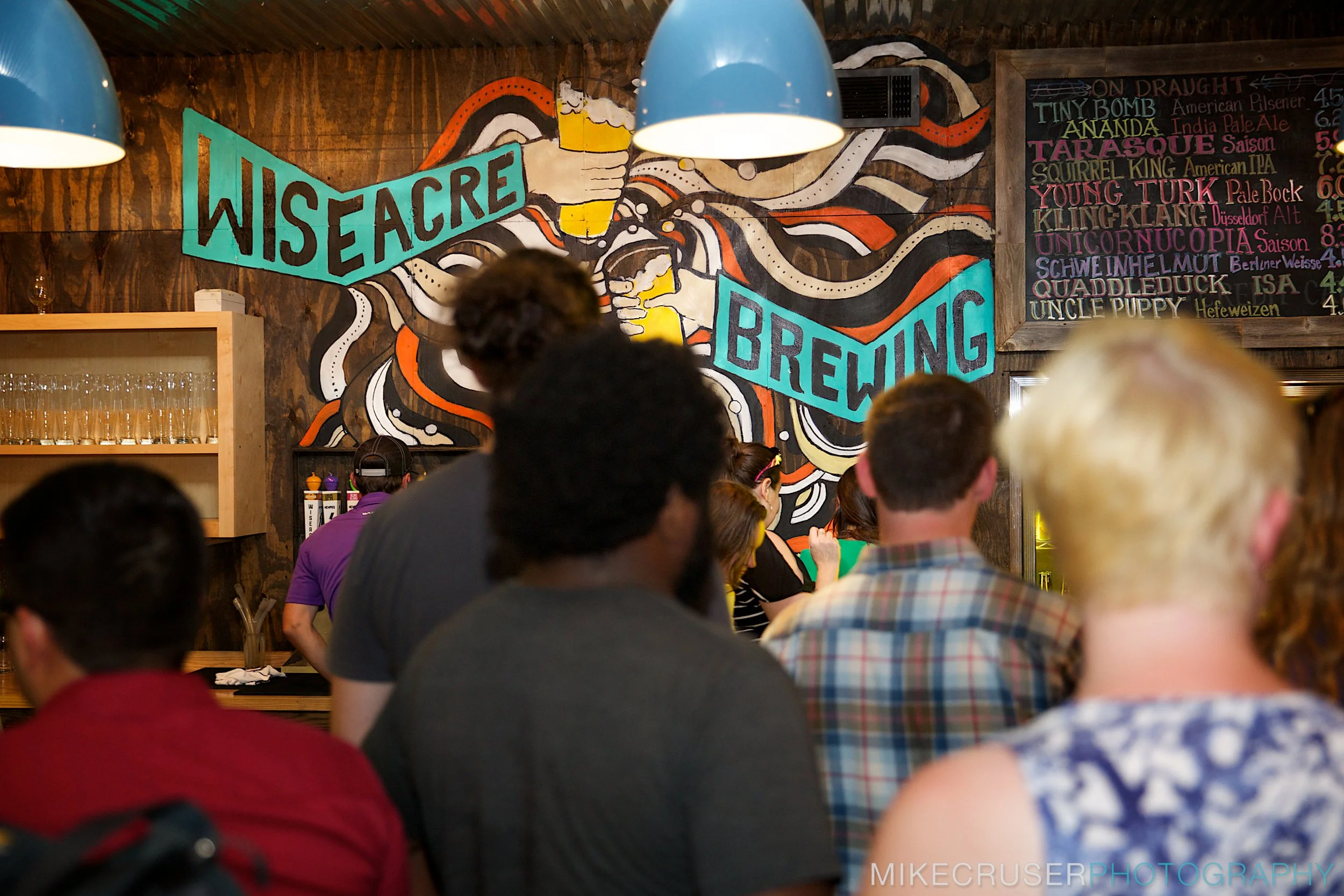 Slowpoke Studio’s website redesign for Wiseacre Brewing Company. People standing in line at Wiseacre Brewing Co. with a colorful mural and a chalkboard menu in the background.