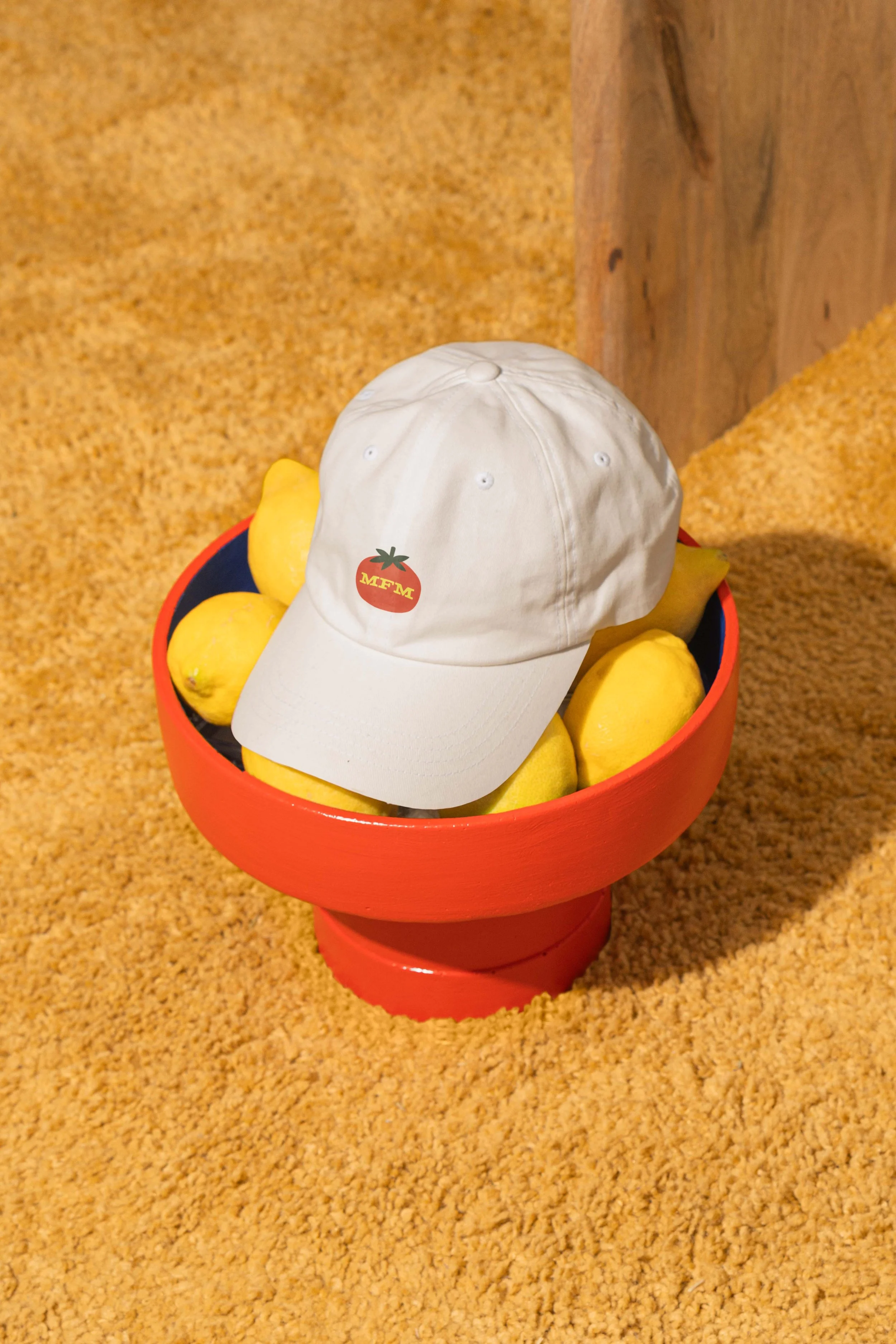 Slowpoke Studio refreshed the Memphis Farmers Market merch design adding anew revenue stream. white baseball cap featuring a MFM tomato logo on top, placed on a bowl of lemons