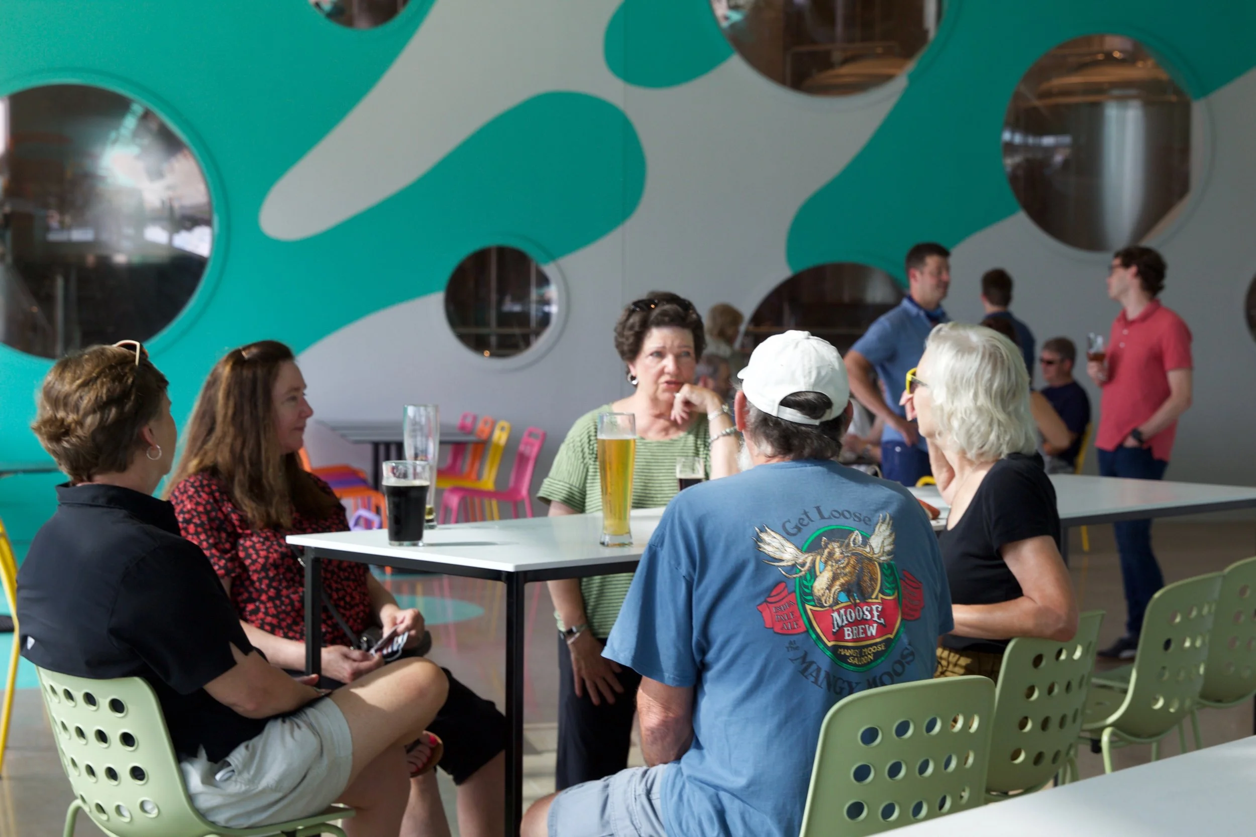 Slowpoke Studio’s website redesign for Wiseacre Brewing Company. Group of five people sitting and talking at a table with drinks in a modern indoor space.