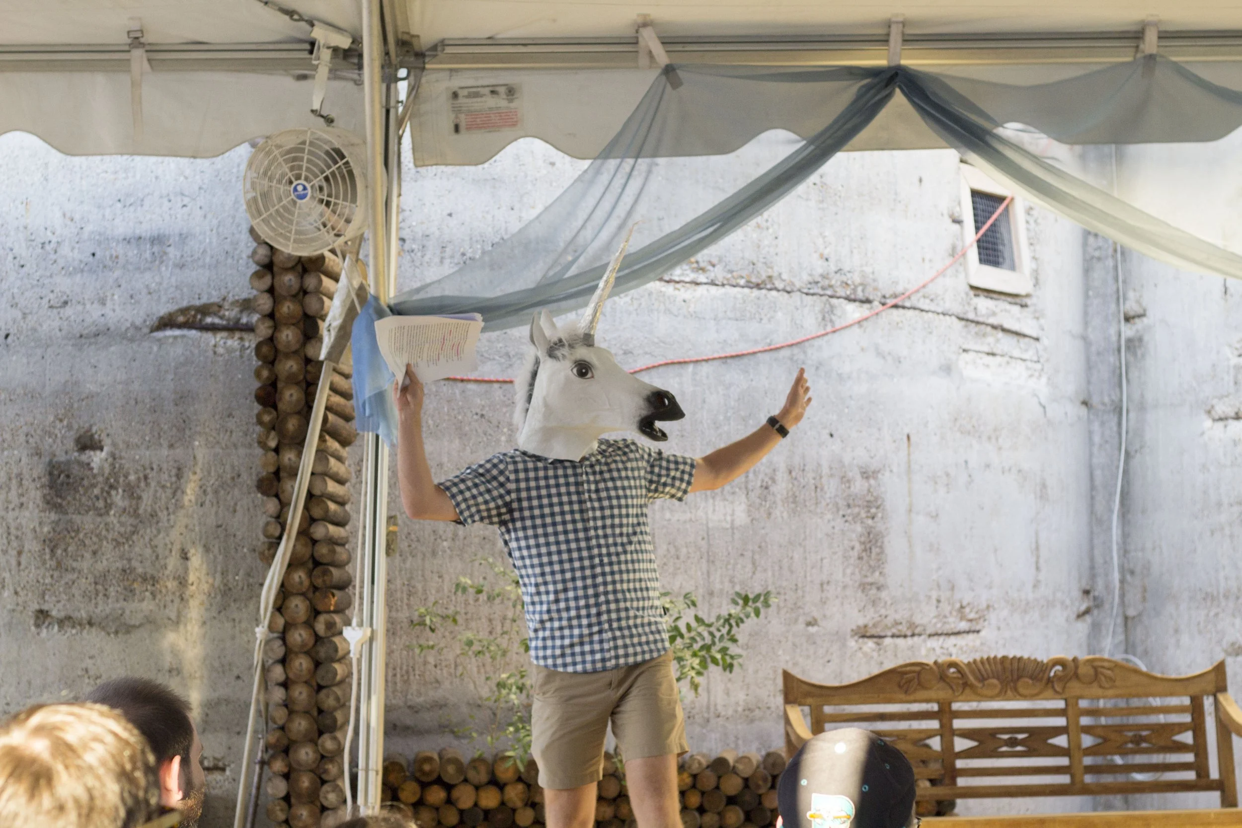 Slowpoke Studio’s website redesign for Wiseacre Brewing Company. Person wearing a unicorn mask, holding a book in one hand, and gesturing with the other, standing in front of a small crowd under a tent.