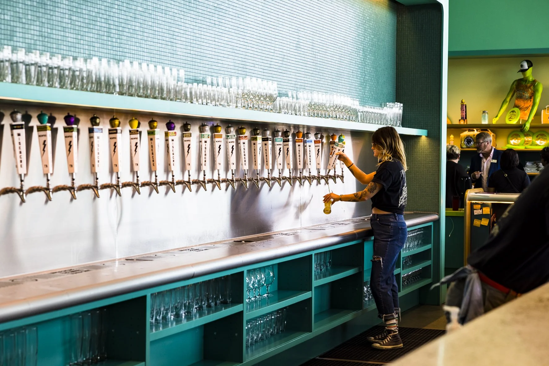 Slowpoke Studio’s website redesign for Wiseacre Brewing Company.  A woman with tattoos filling a glass at a bar with multiple beer taps in a vibrant, colorful environment.