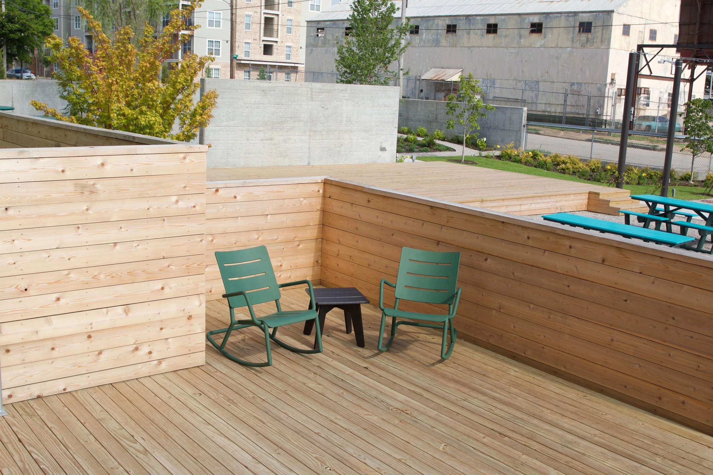 Slowpoke Studio’s website redesign for Wiseacre Brewing Company. Wooden deck with two green patio chairs and a small black side table, surrounded by wooden privacy walls, with trees and buildings in the background.