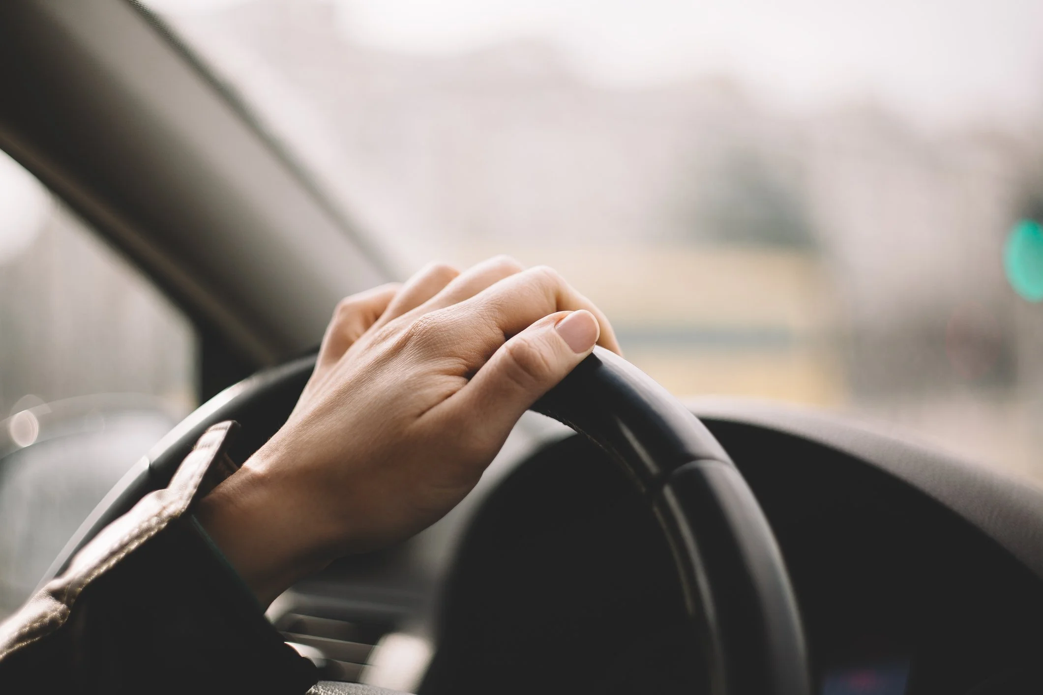 Close-up of a person's hand on a car steering wheel inside a vehicle.