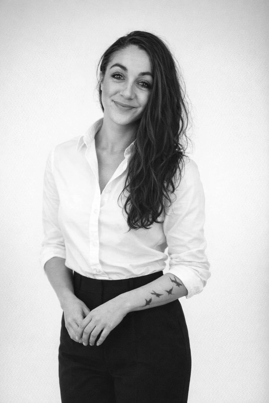 Black and white photo of a woman sitting on a bench, looking away, with a shadow cast on the wall behind her in a modern interior.