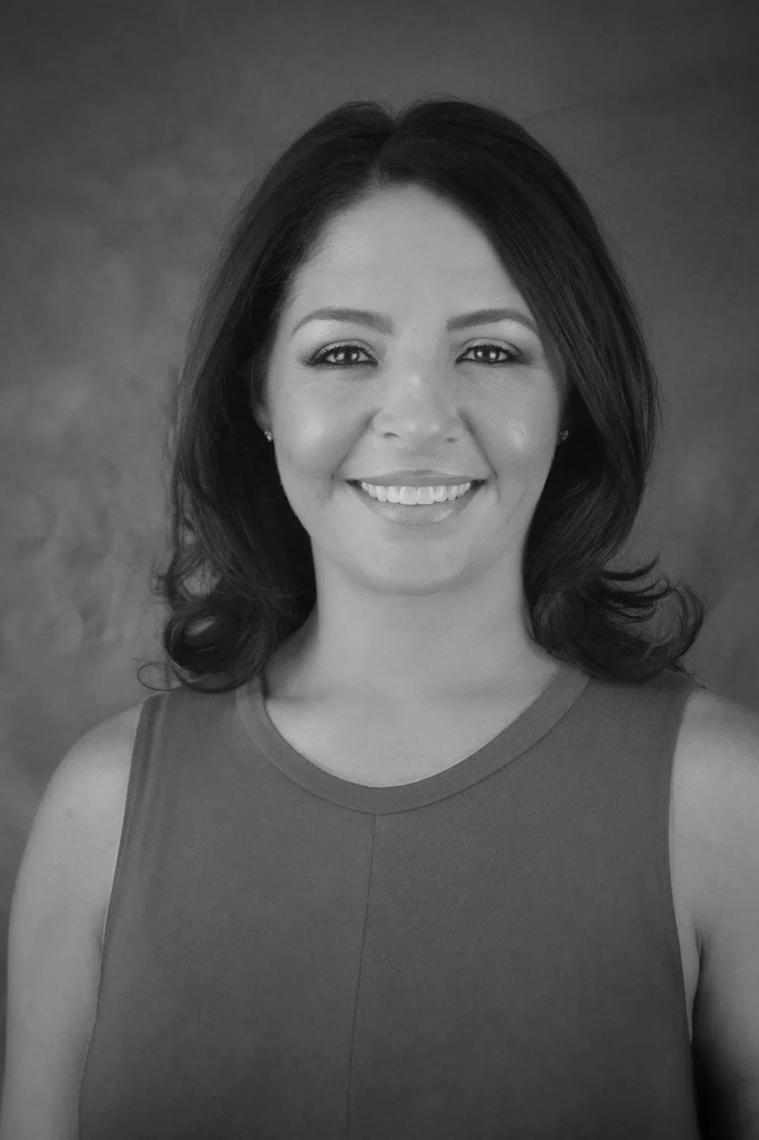 Black and white portrait of a woman with shoulder-length hair, smiling, wearing a sleeveless top.