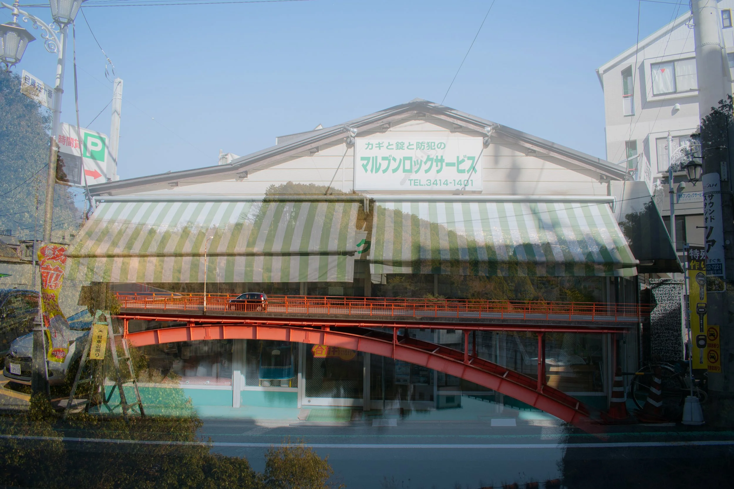 Japan double exposure film photo of orange bridge with car on it overlaid with store front.