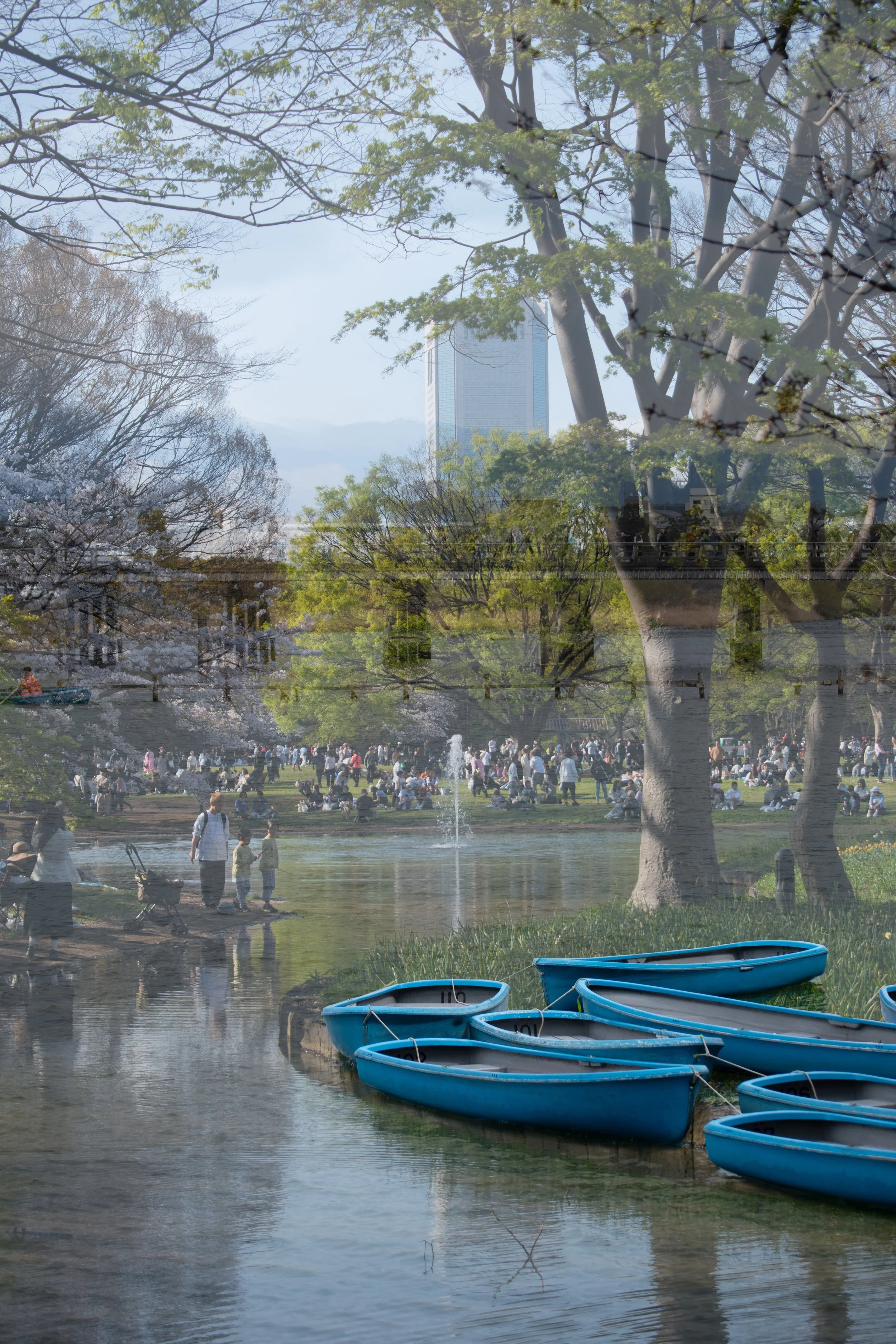 Japan double exposure film photo of blue personal boats with a dock overlaid on top of park fountain and crowd.