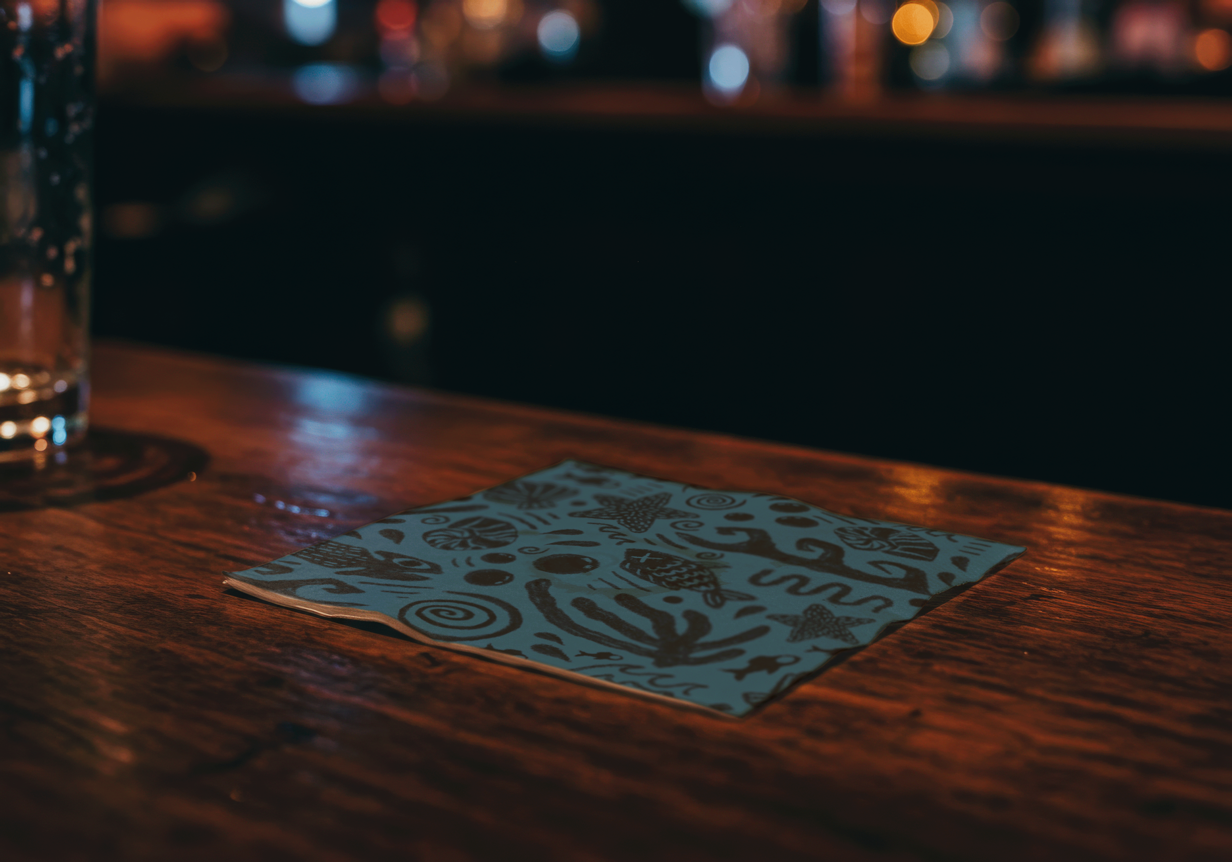 LURK coasters depicting folk stylized Chupacbra napkin on bar surface.