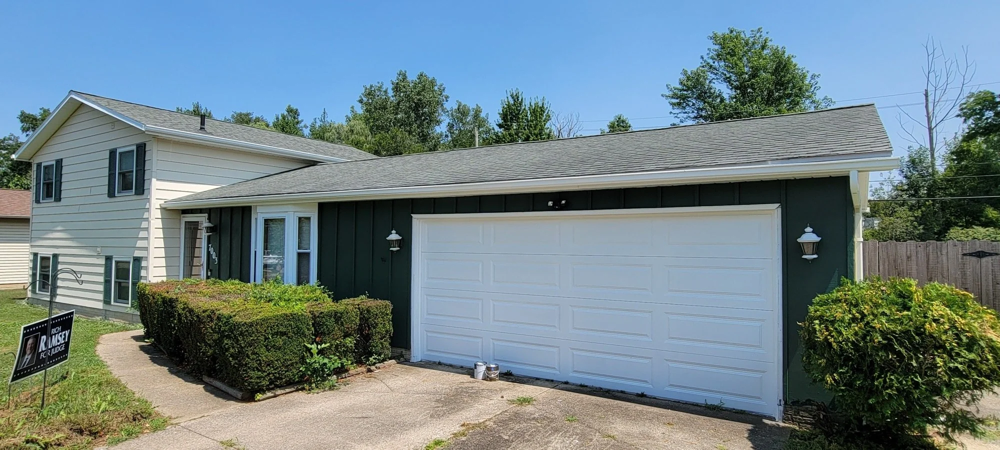 A residential house with attach garage, greenery, and a "Ruch Ramsey for Judge" political sign in the yard.