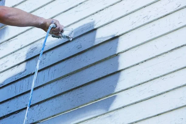 Person using a hose to spray water on horizontal white wooden siding of a house.