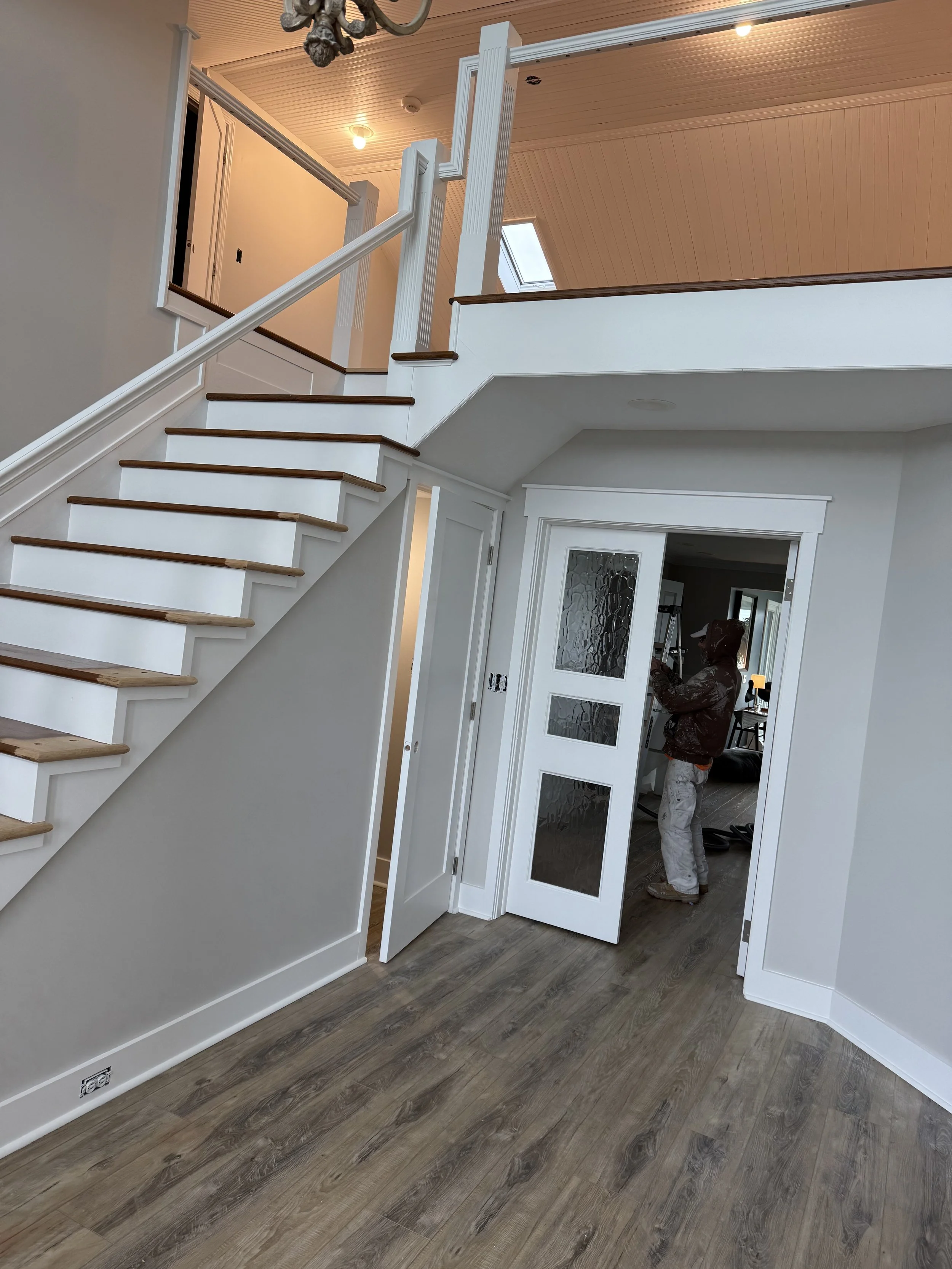 Interior of a house with a staircase and a person working near some doors.