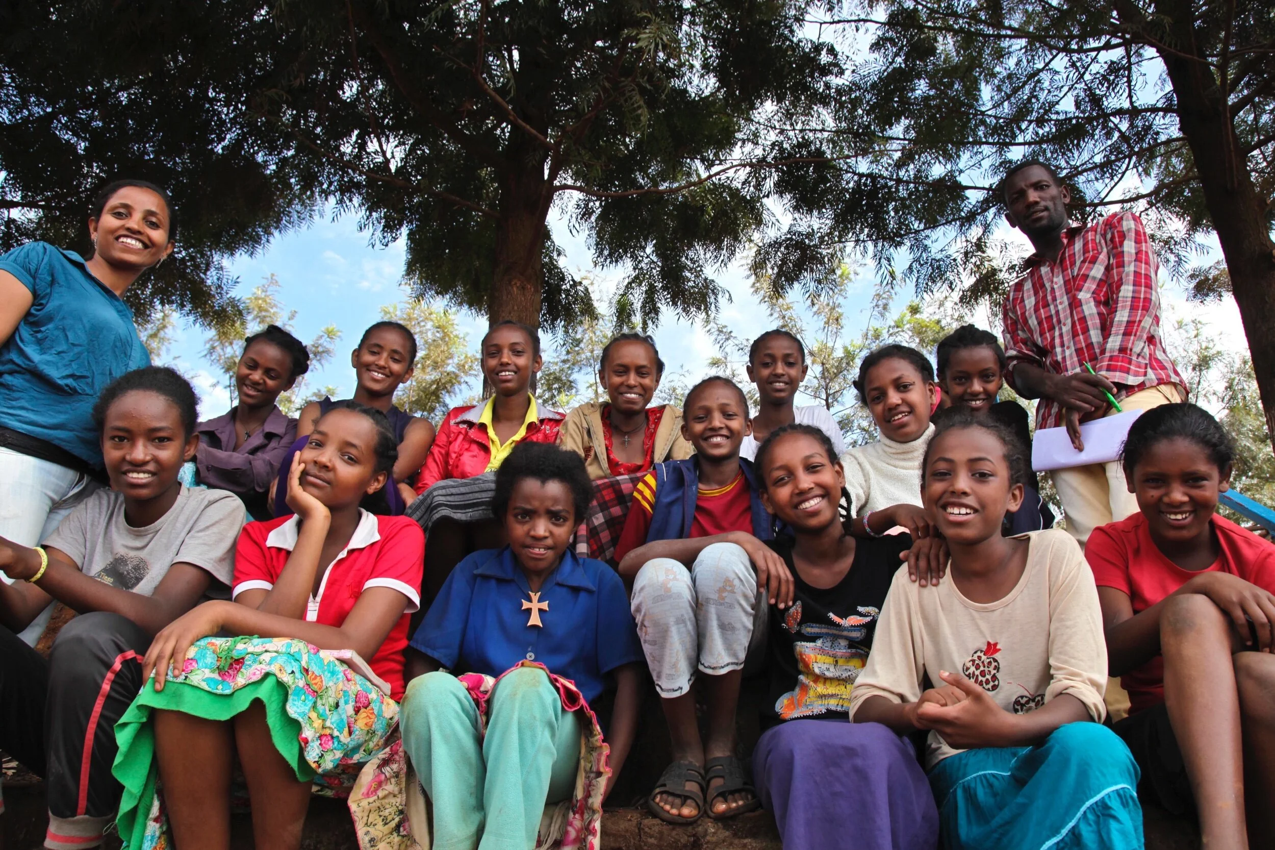 Ethiopian girls sitting under a tree wearing bright clothing and smiling together