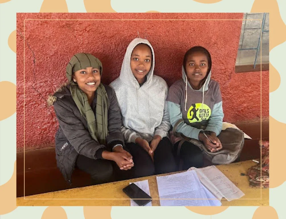 Athletic Scholar Diborah sitting with 2 classmates on a bench with class material at table in front of them