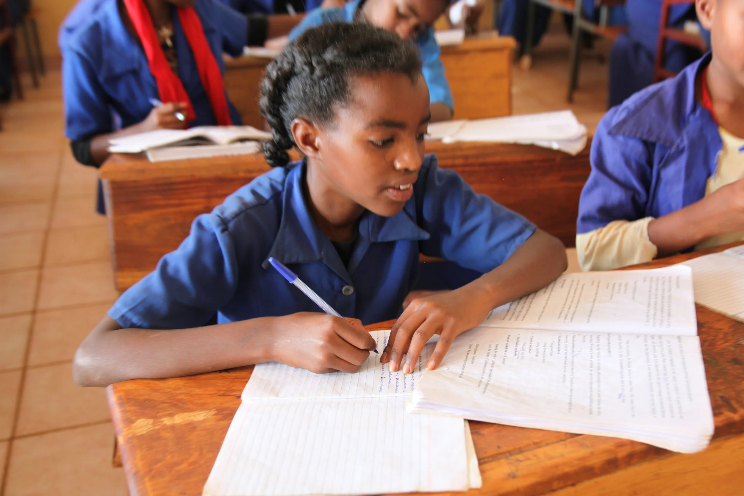 Ethiopian girl at school sitting at a desk writing notes while looking at text