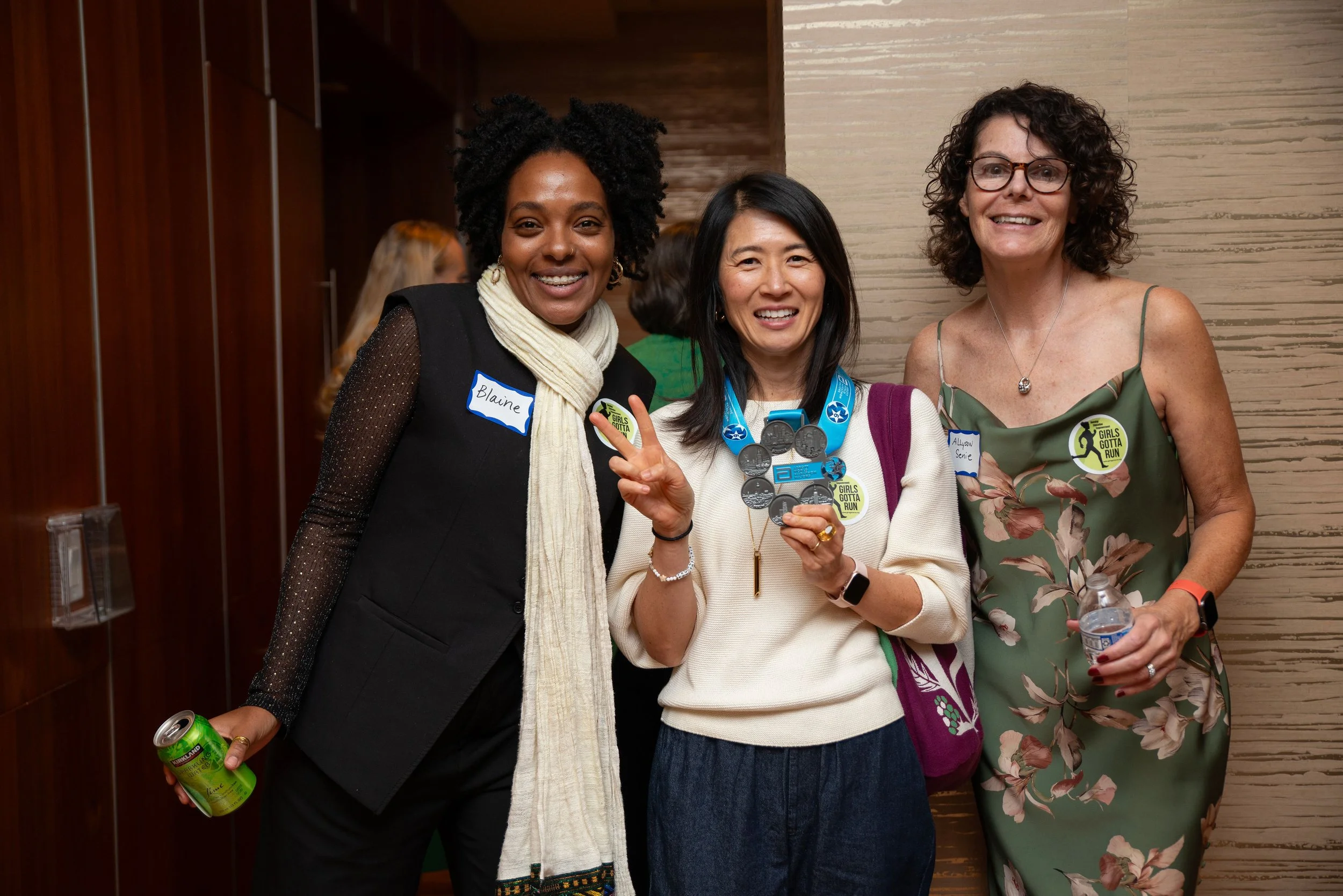3 women standing together at an event wearing Girls Gotta Run stickers and nametags