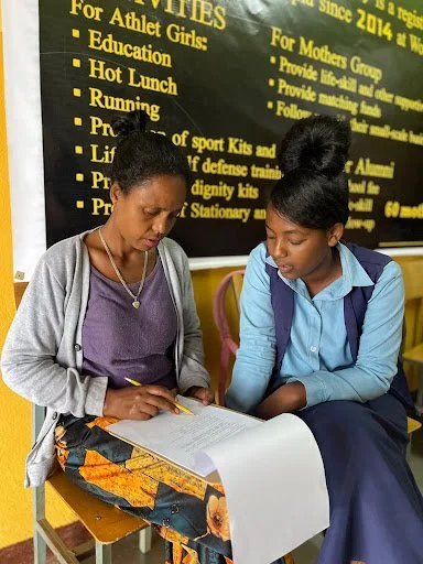 Athletic Scholar sitting with her mother who is pointing her pencil at paper on a clip board