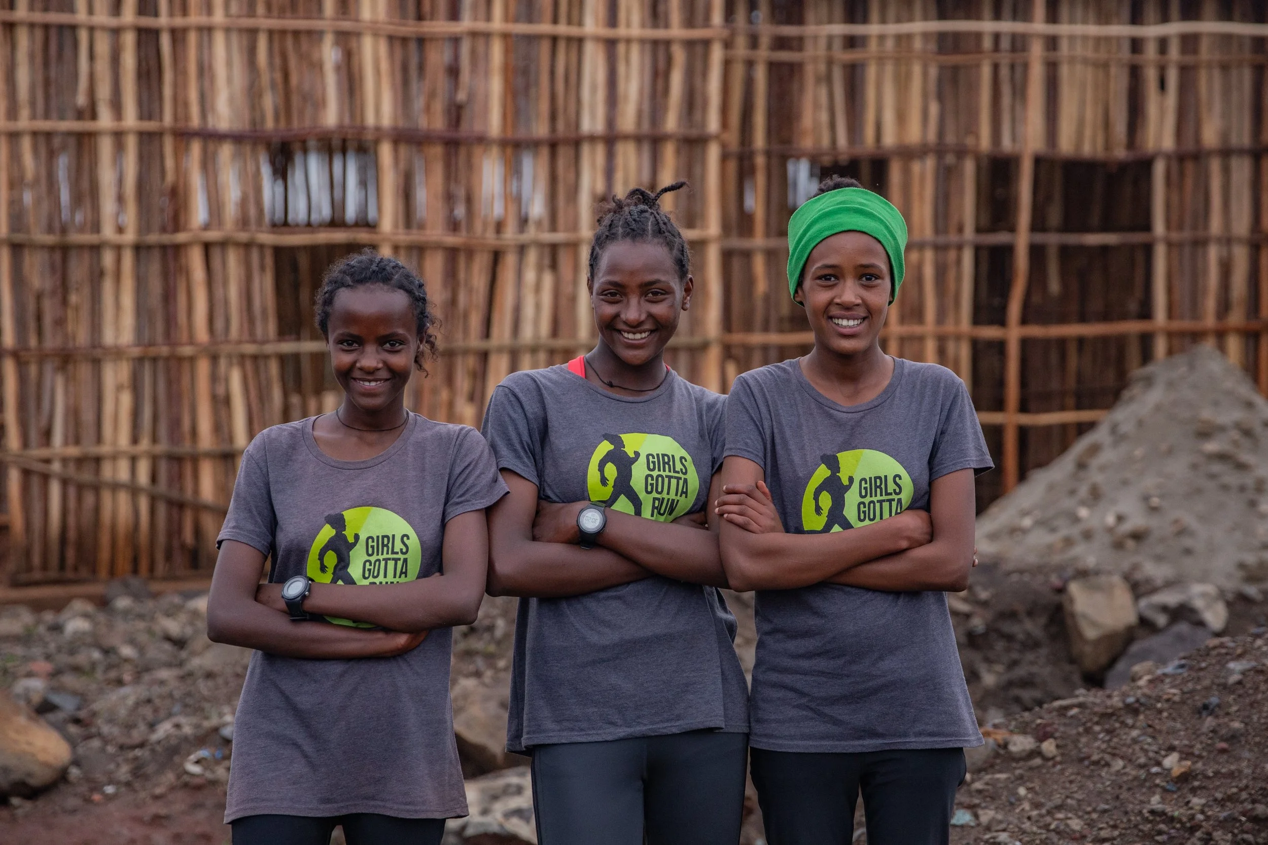 Three Ethiopian teen girls standing together smiling with arms confidently crossed wearing Girls Gotta Run shirts