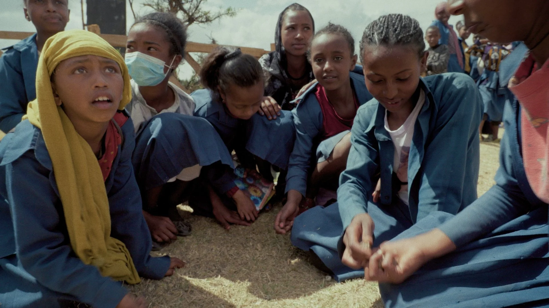 Young ethiopian girls in school uniforms crouched in a circle together outside playing a dice game
