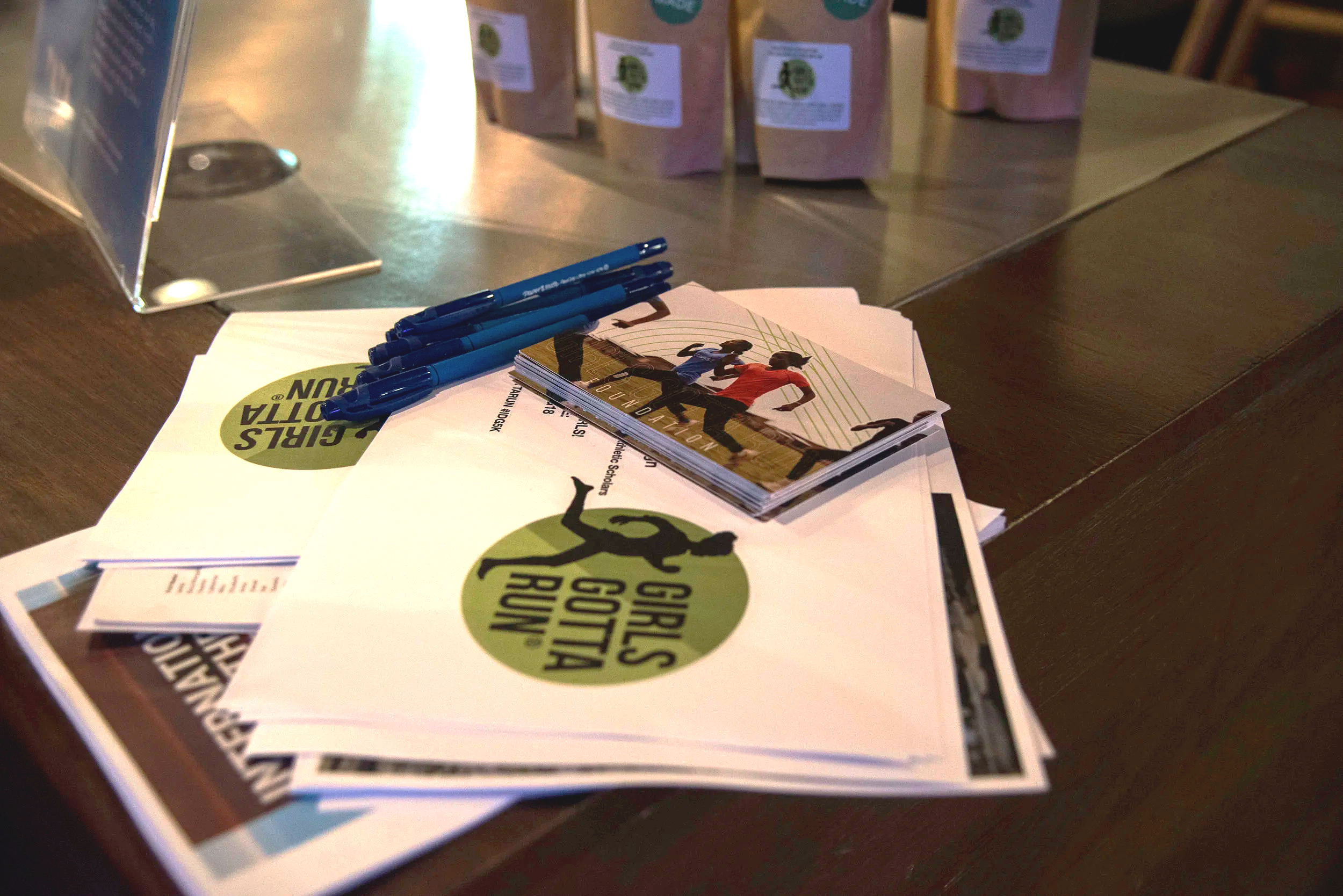 Girls Gotta Run branded flyers, postcards, coffee bags and pens arranged on a table
