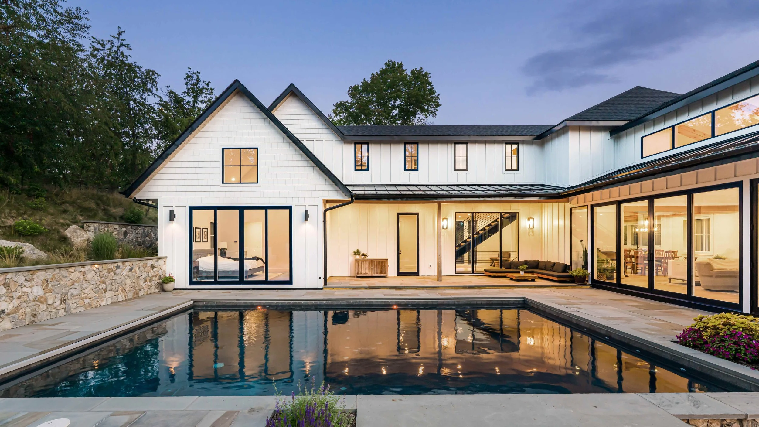 Modern house with large glass windows, a backyard with a swimming pool, outdoor seating, and garden decor