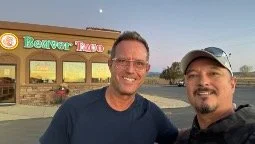 Two men smiling in front of a building with a sign that reads 'Beacon Taps'