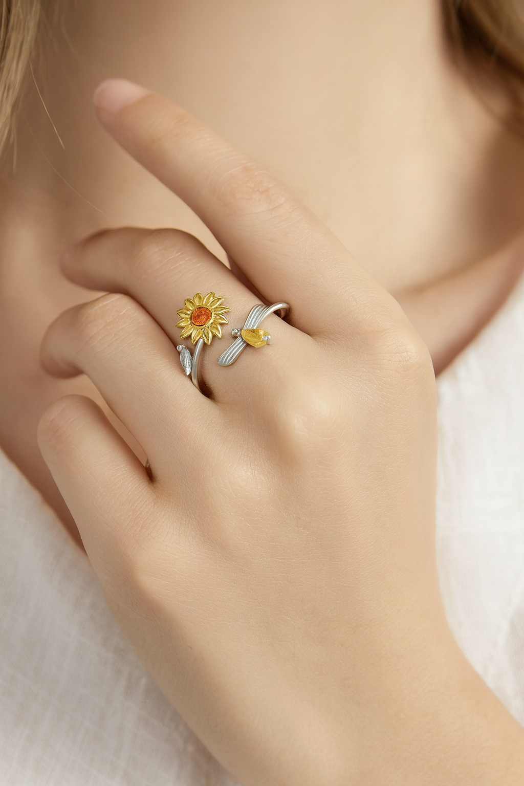 Close-up of a hand with two rings, one with a sunflower design and a yellow gemstone, and the other with a silver band and a gold arrow detail, resting near the face.