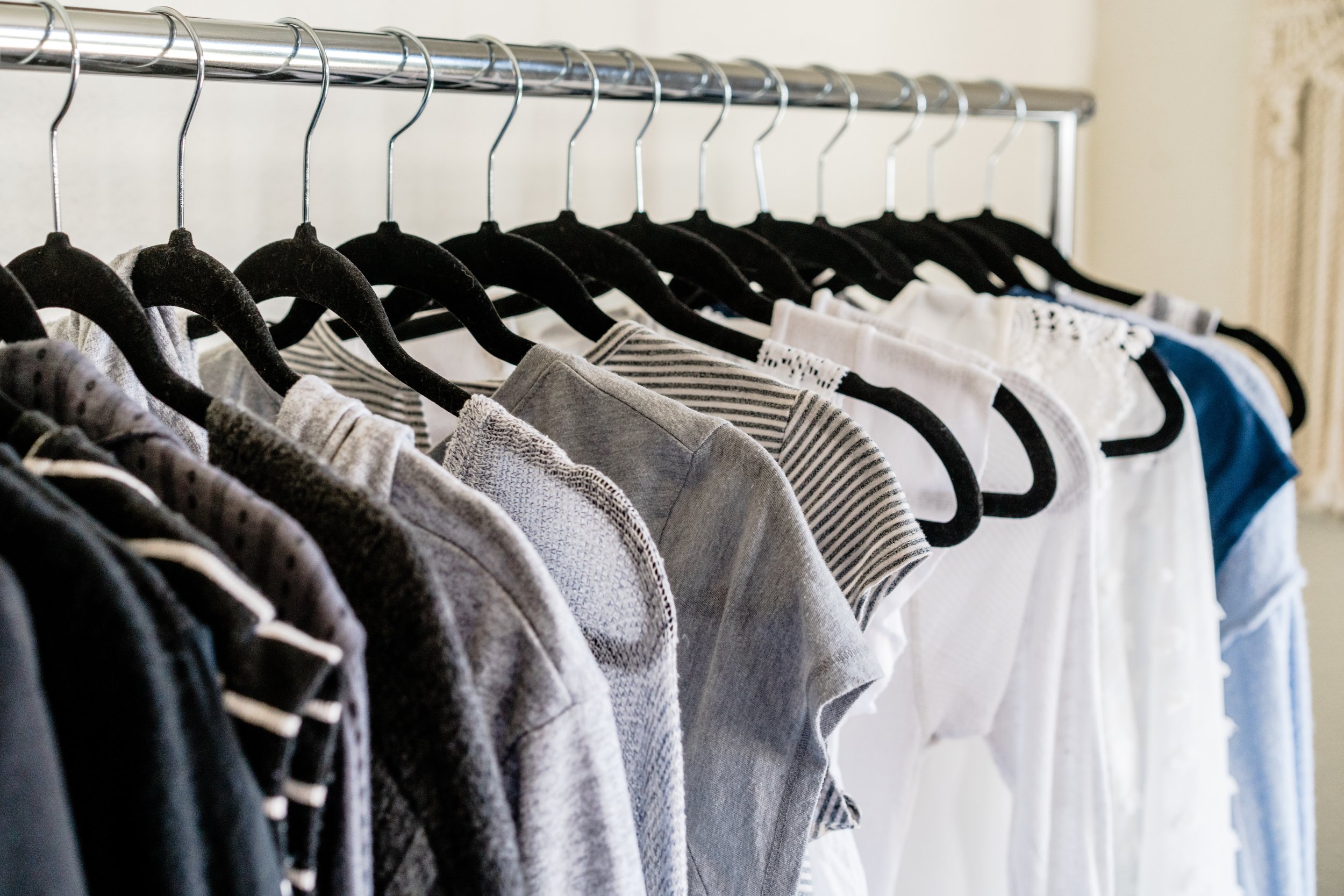 A row of various casual T-shirts on black hangers hanging on a metal clothing rack.