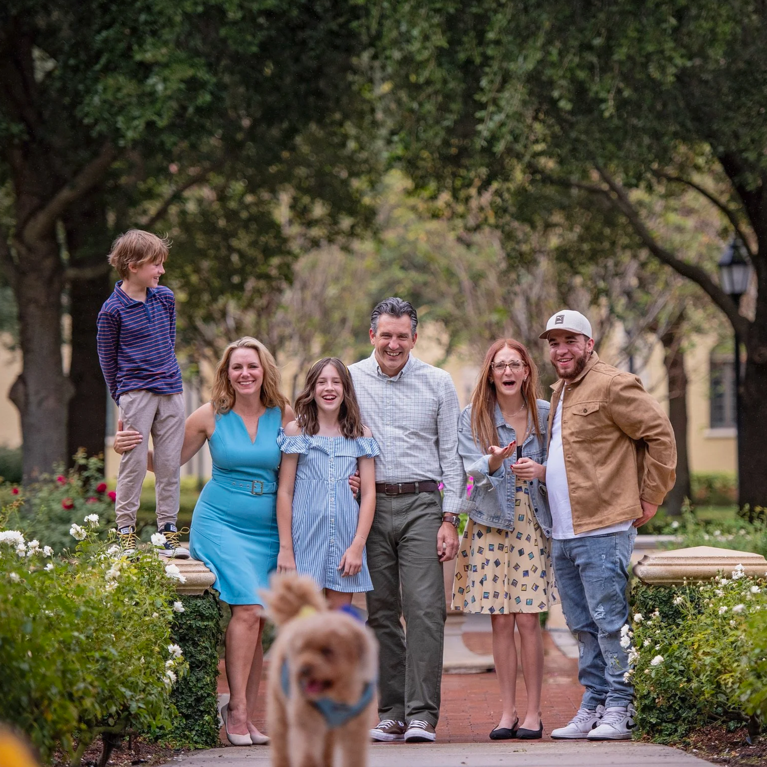Family enjoying time together outdoors in a park with trees and flowers, walking and smiling.