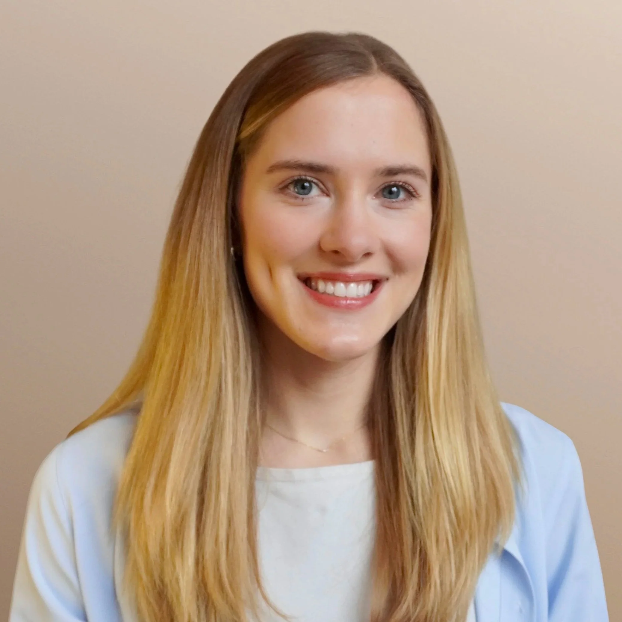Headshot of a young woman with long blonde hair, blue eyes, smiling, against a beige background.