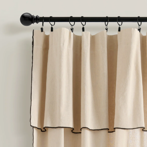 Beige curtains hanging on a black curtain rod with rings.