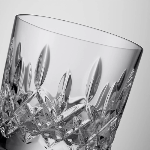 Close-up of a clear cut crystal glass with intricate patterns, tilted against a plain light gray background.