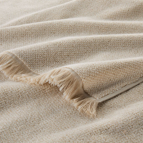Close-up of a beige textured fabric blanket with fringed edges, draped over a surface.
