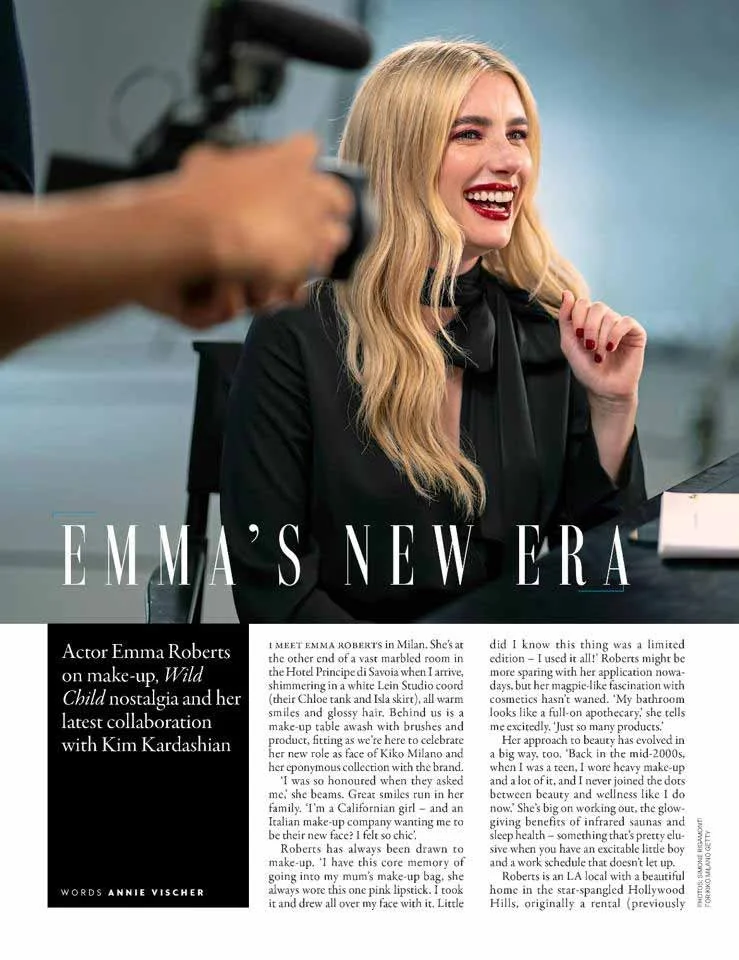 A woman with long blonde hair and red lipstick smiling at a photoshoot.