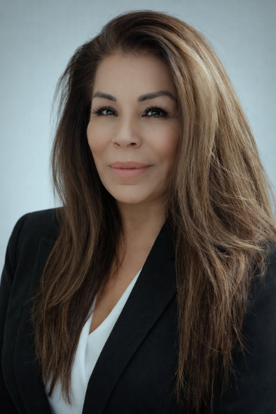 Professional woman with long, wavy hair wearing a black blazer and white shirt, smiling softly at the camera.