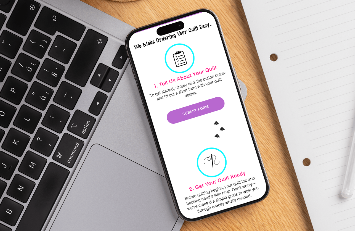 Smartphone on a wooden desk displaying a quilting order form app with steps to about your quilt and get your quilt ready, alongside a laptop, notebook, and pen.