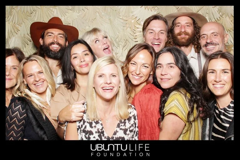 Group of people smiling and posing together for a photo, with a beige patterned background, at an Ubuntu Life Foundation event.