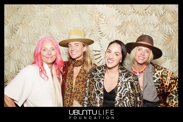 Four women dressed in leopard print, animal print, and Western-style clothing, wearing wide-brimmed hats, smiling at a photo booth with a decorative leaf-patterned background, at an event for the Ubuntu Life Foundation.