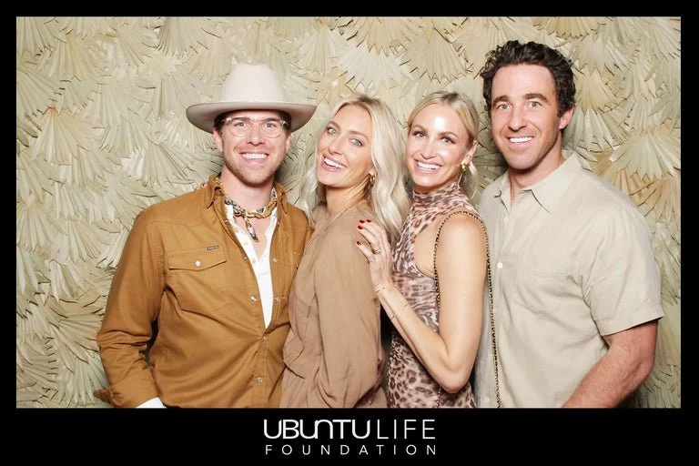 Four people smiling and posing together in front of a beige, textured background at an event for the Ubuntu Life Foundation.
