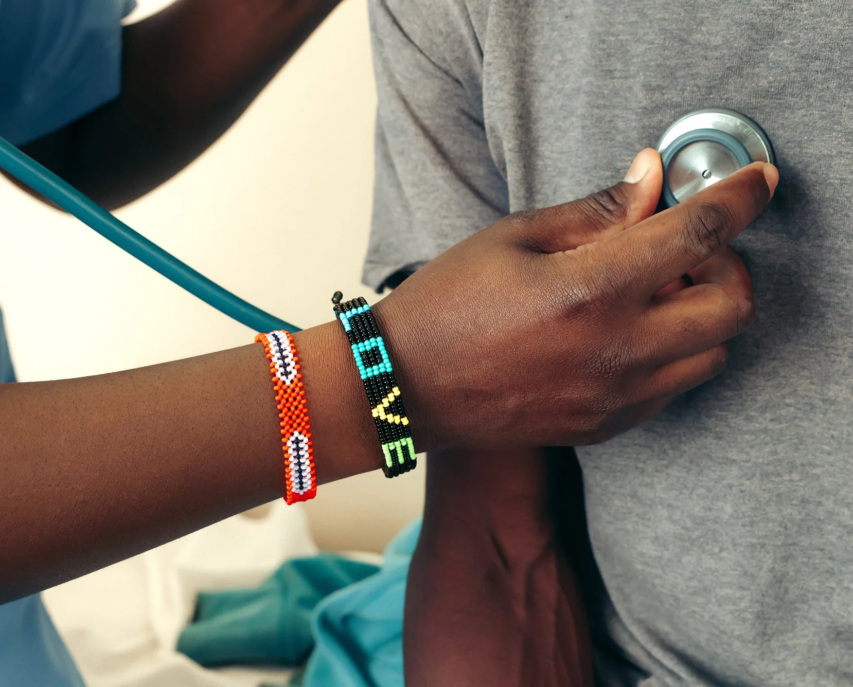 A healthcare worker uses a stethoscope on a patient, wearing colorful beaded bracelets on their wrist.