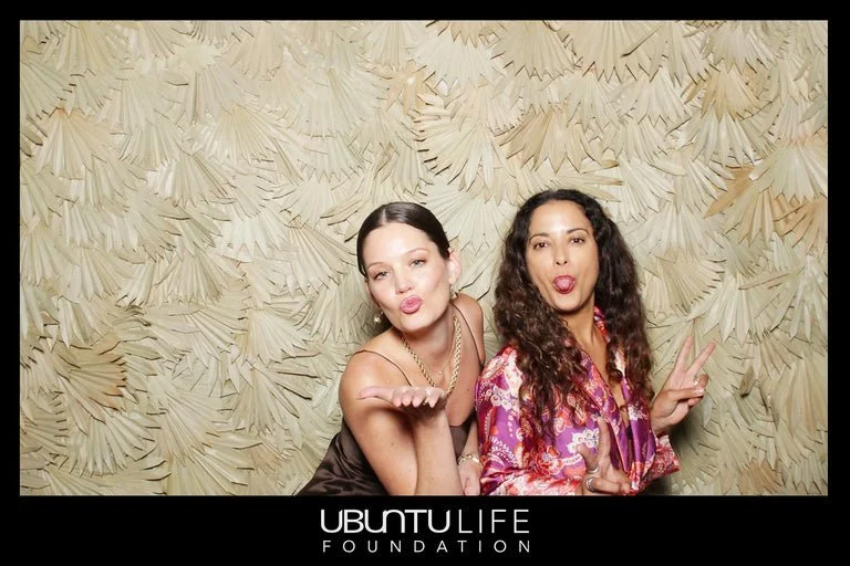 Two women posing playfully in front of a textured beige background, with the Ubuntu Life Foundation logo at the bottom.