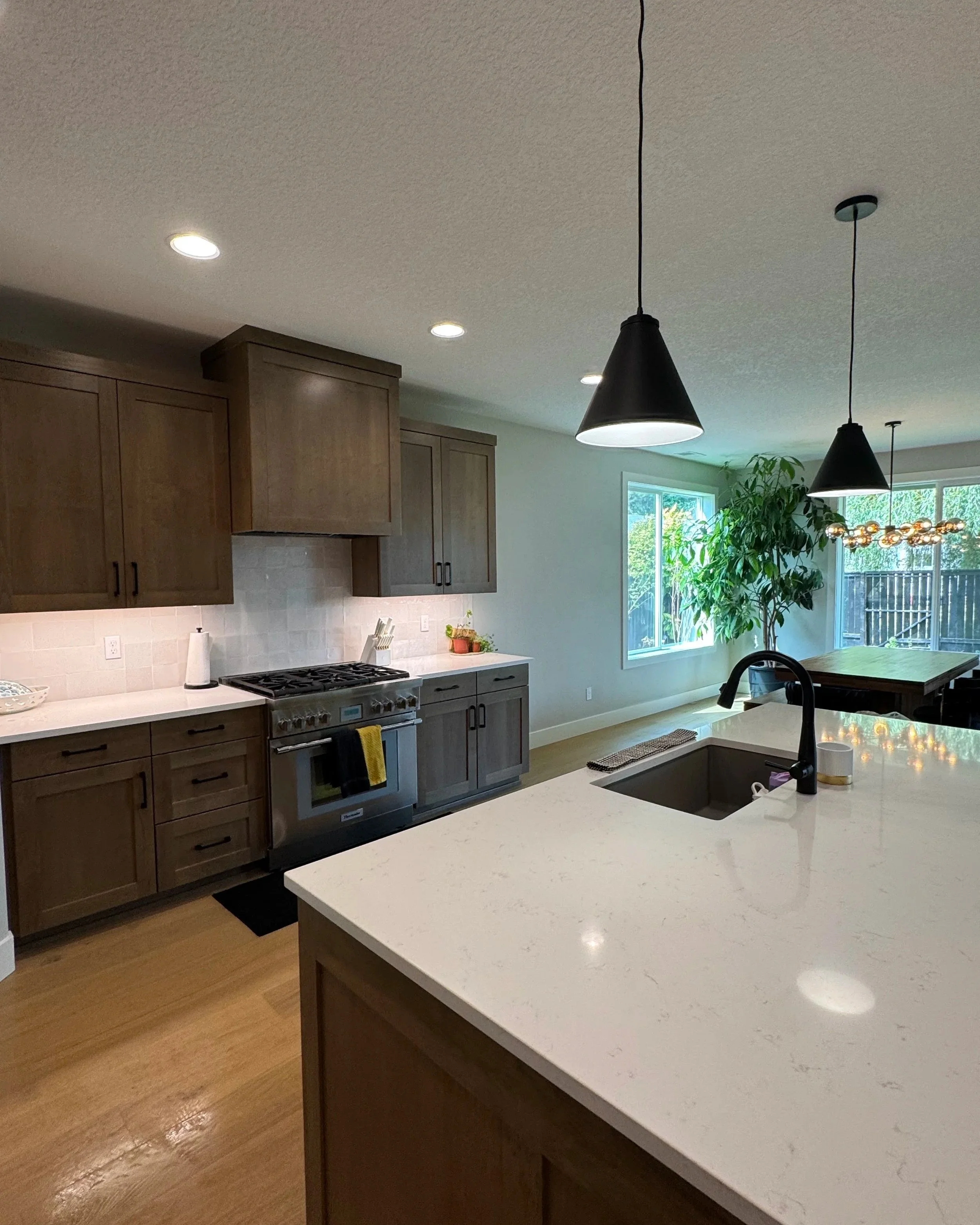 Modern kitchen with wooden cabinets, white countertops, modern stainless steel stove, black faucet, and a large window with a green plant nearby.