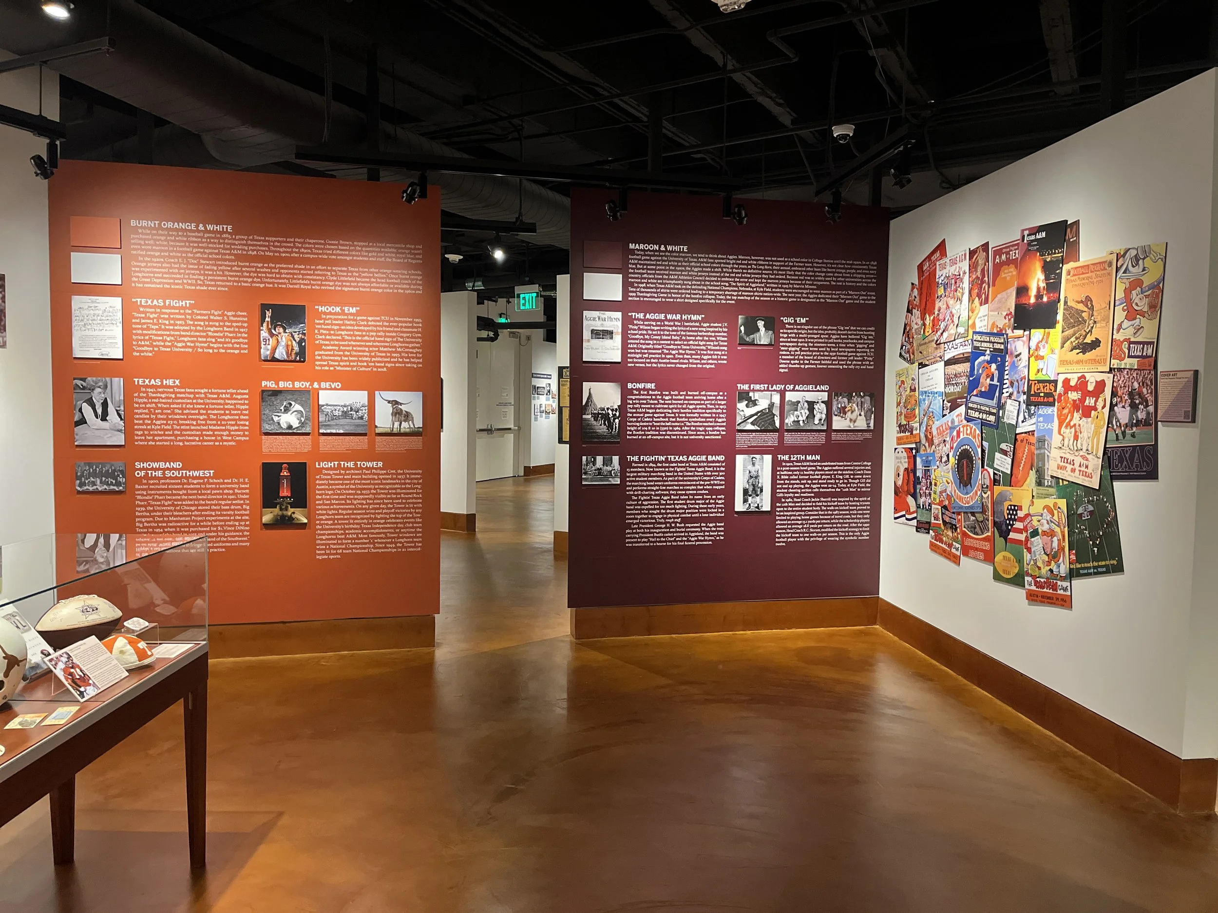 Exhibit in a museum with orange and maroon informational panels and a display of vintage Texas Longhorn football gameday programs.