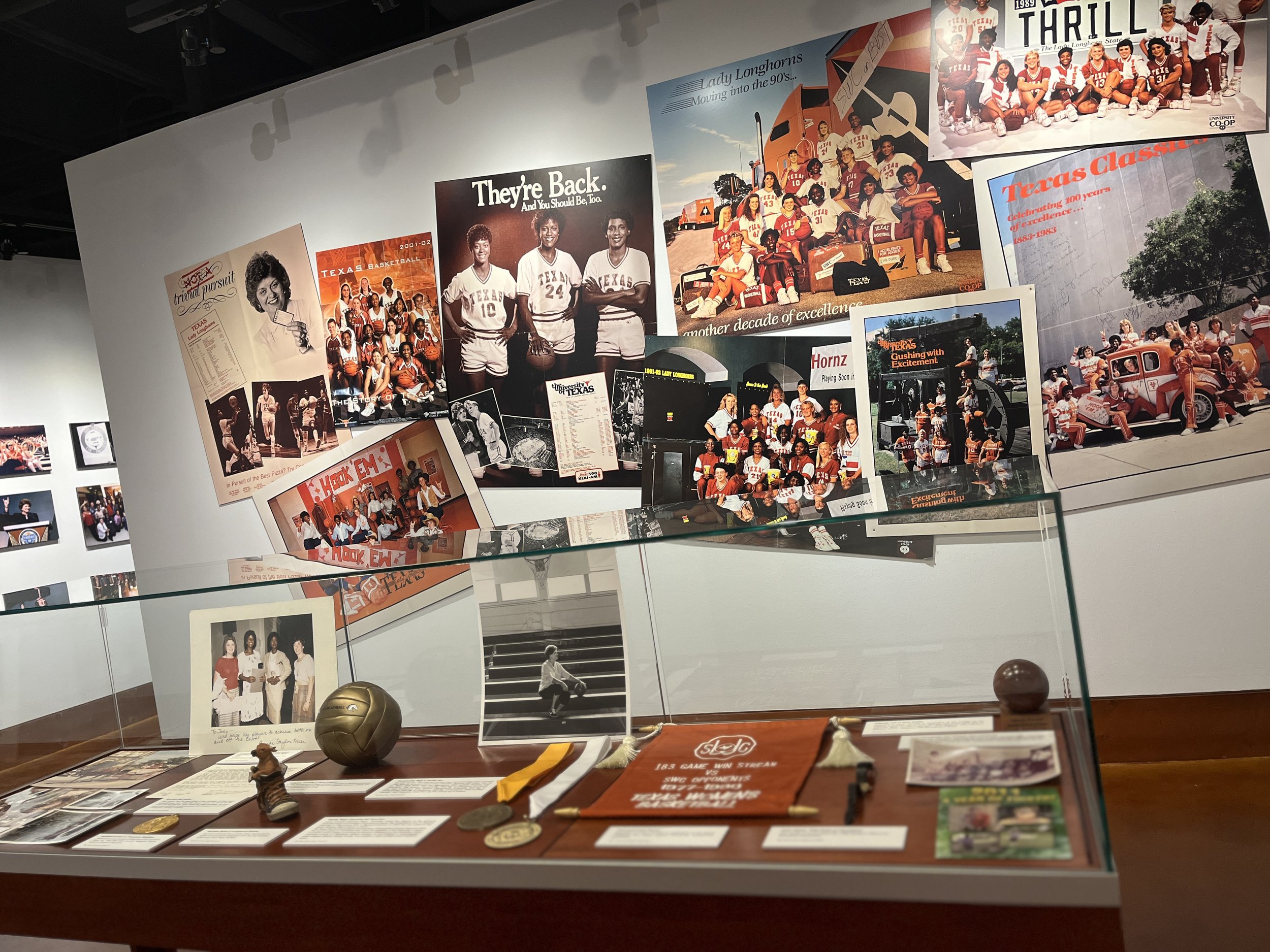 Museum exhibit featuring vintage Texas Longhorns sports memorabilia, photos of teams and players, and related artifacts displayed in glass case.