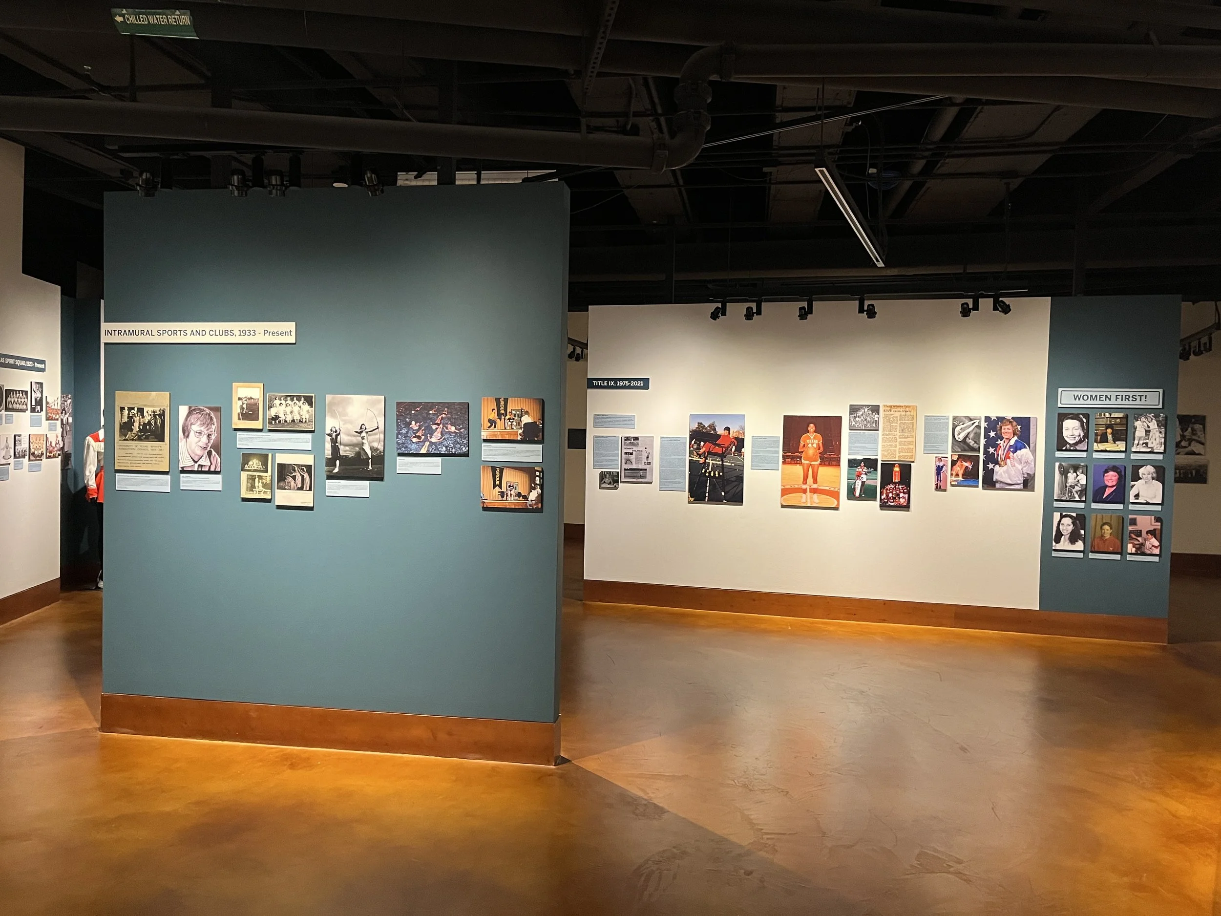 Exhibit display in a museum with photos and text panels about intramural sports and clubs from 1933 to the present, and women first! themed display on the right side.